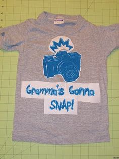 a t - shirt with the words grandma's camera snap on it, sitting on a cutting board