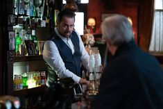 a man standing at a bar with a glass in his hand next to another man