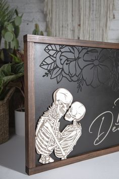 a wooden sign with a skeleton holding a woman's head in front of flowers