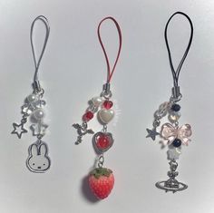 three necklaces with charms attached to them on a white surface, one has a strawberry and the other has an animal charm