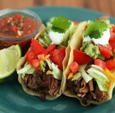 three tacos on a green plate with salsa and avocado garnish