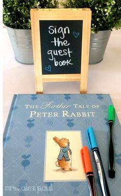 there is a book and pens on the table next to each other with a chalkboard in front of it