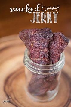 a jar filled with smoked beef next to a wooden table and text overlay that reads smokey beef jerry