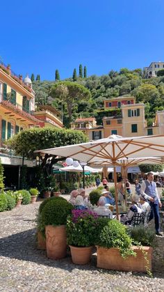 people sitting at tables under umbrellas in the middle of an open area with potted plants