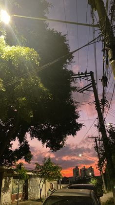 a car parked on the side of a road under power lines and trees at sunset