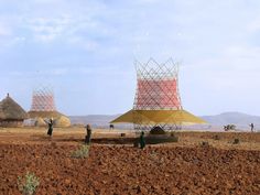 some people are standing in the middle of an open field with three large structures on top of them