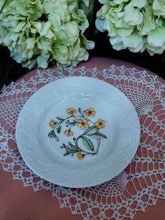 a white plate sitting on top of a doily next to some green and yellow flowers