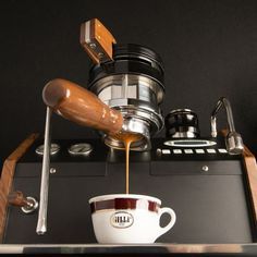 coffee being poured into a white cup on top of an espresso machine with wooden spoons