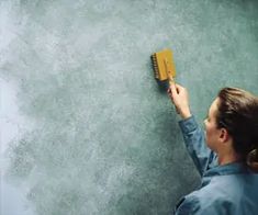 a woman is painting a wall with gray paint and a yellow brush in her hand