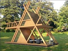 a large wooden structure sitting in the middle of a grass covered field next to trees