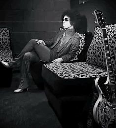 a man sitting on top of a couch next to a guitar in a black and white photo