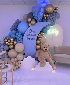 a teddy bear sitting in front of a balloon arch with balloons on it and a sign that says, over the moon for you