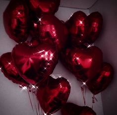 red heart shaped balloons in the shape of hearts with sparkles on them, hanging from a wall