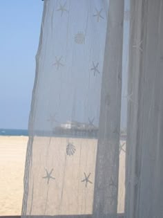 an open window with white sheer curtains on the beach