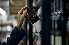 a person holding a bottle of wine in front of a wall with pictures on it