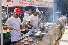 two men grilling hamburgers on an outdoor grill with red and white umbrellas