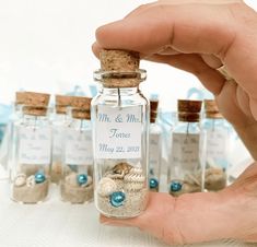 a hand holding a tiny bottle filled with sand and shells