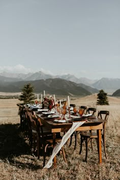 a long table set with place settings in the middle of an open field surrounded by mountains