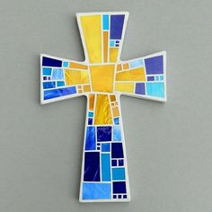 a cross made out of stained glass on a gray surface with blue and yellow squares