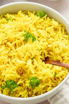 a white bowl filled with yellow rice and broccoli on top of a table