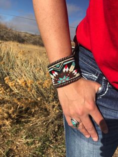 a person wearing a red shirt and blue jeans with a bracelet on their wrist in the middle of a field