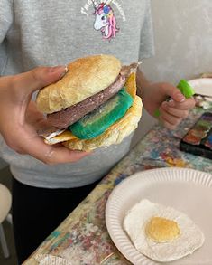 a person holding a sandwich in front of a plate with an egg on the side