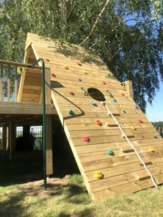 a wooden climbing wall in the shape of a house with a slide on it's side