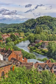 a river running through a lush green countryside next to tall buildings and forest covered hills