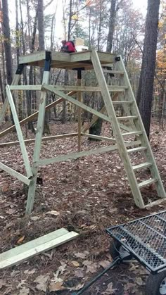 a wooden swing set in the woods with some tools on the ground next to it