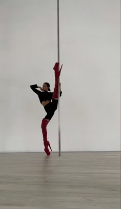 a woman standing on one leg and holding onto a pole while wearing red boots, in front of a white wall