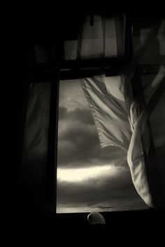 a black and white photo of an american flag in front of a window with curtains