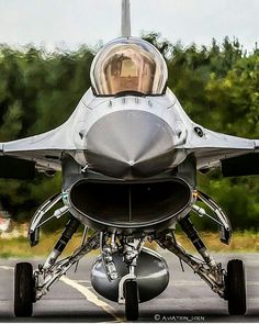 a jet fighter sitting on top of an airport tarmac with trees in the background