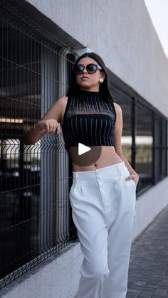 a woman standing next to a building wearing white pants and a cropped black top