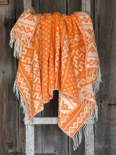 an orange and white blanket sitting on top of a wooden chair next to a wall