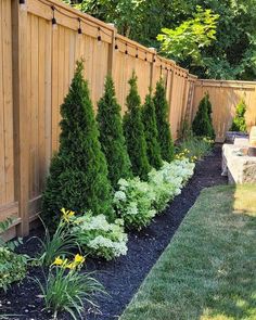 a garden with trees and shrubs in the middle of it, along side a wooden fence