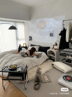 a woman laying in bed with a record player on the floor and a cat sitting next to her