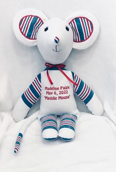 a white stuffed animal with blue and red stripes on it's body sitting on a bed