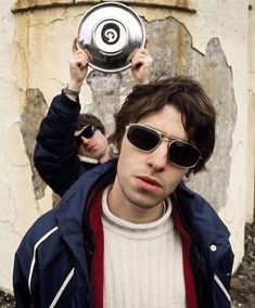 a man in sunglasses holding up a silver object above his head with two other men behind him