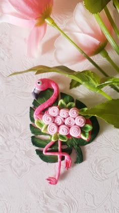 a pink flamingo brooch sitting on top of a table next to some flowers