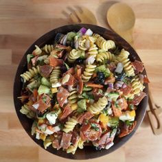 a wooden bowl filled with pasta salad on top of a table next to utensils