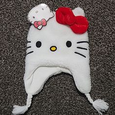 a white hello kitty hat with a red bow on it's head sitting on the carpet