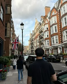 two people walking down the sidewalk in front of some cars and buildings with a british flag on it