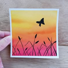 a person holding up a card with a painting of a butterfly flying over the grass