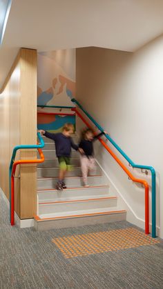 two children are climbing up the stairs in an office building with painted walls and flooring