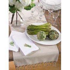 asparagus and artichokes on a white plate next to wine glasses