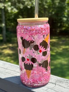 a pink cup with mickey mouse on it sitting on a wooden table in front of some trees