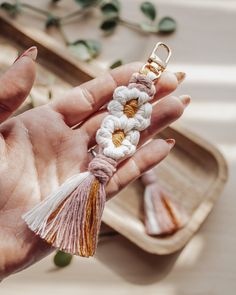 a hand holding a keychain with flowers and tassels attached to it