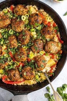 a skillet filled with meatballs and rice topped with green onions, bell peppers and jalapenos