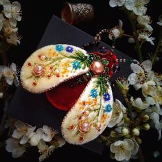 two pieces of jewelry sitting on top of a table next to some flowers and a vase