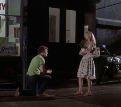 a man kneeling down next to a woman in front of a store window at night